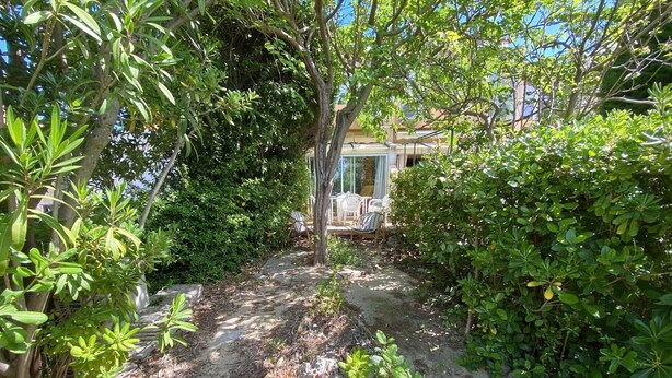 A garden pathway leading to a seating area with chairs, surrounded by dense foliage and trees. - "Le Maddy" studio garden-wifi-climate-parking-beach side (Saint-Cyr-sur-Mer)