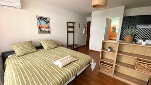 A room with a bed, a hanging light fixture, a painting, and a kitchenette area. - "Le Maddy" studio garden-wifi-climate-parking-beach side (Saint-Cyr-sur-Mer)