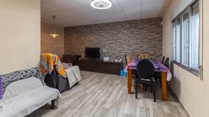 Un salon avec un canapé, une table à manger et des chaises, un téléviseur posé sur un meuble et un mur en briques.