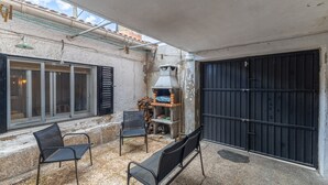 Un espace extérieur aménagé, abrité et doté de chaises, d’un barbecue et offrant une vue sur un bâtiment avec une porte noire.