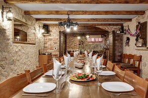 A dining area with a long table set for a meal, wooden chairs, and a stone wall. - Villa Lea Zadarvillas (Nin)
