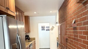 Una cocina con armarios de madera, un refrigerador de acero inoxidable, una pared de ladrillo y una puerta con un cartel de bienvenida.