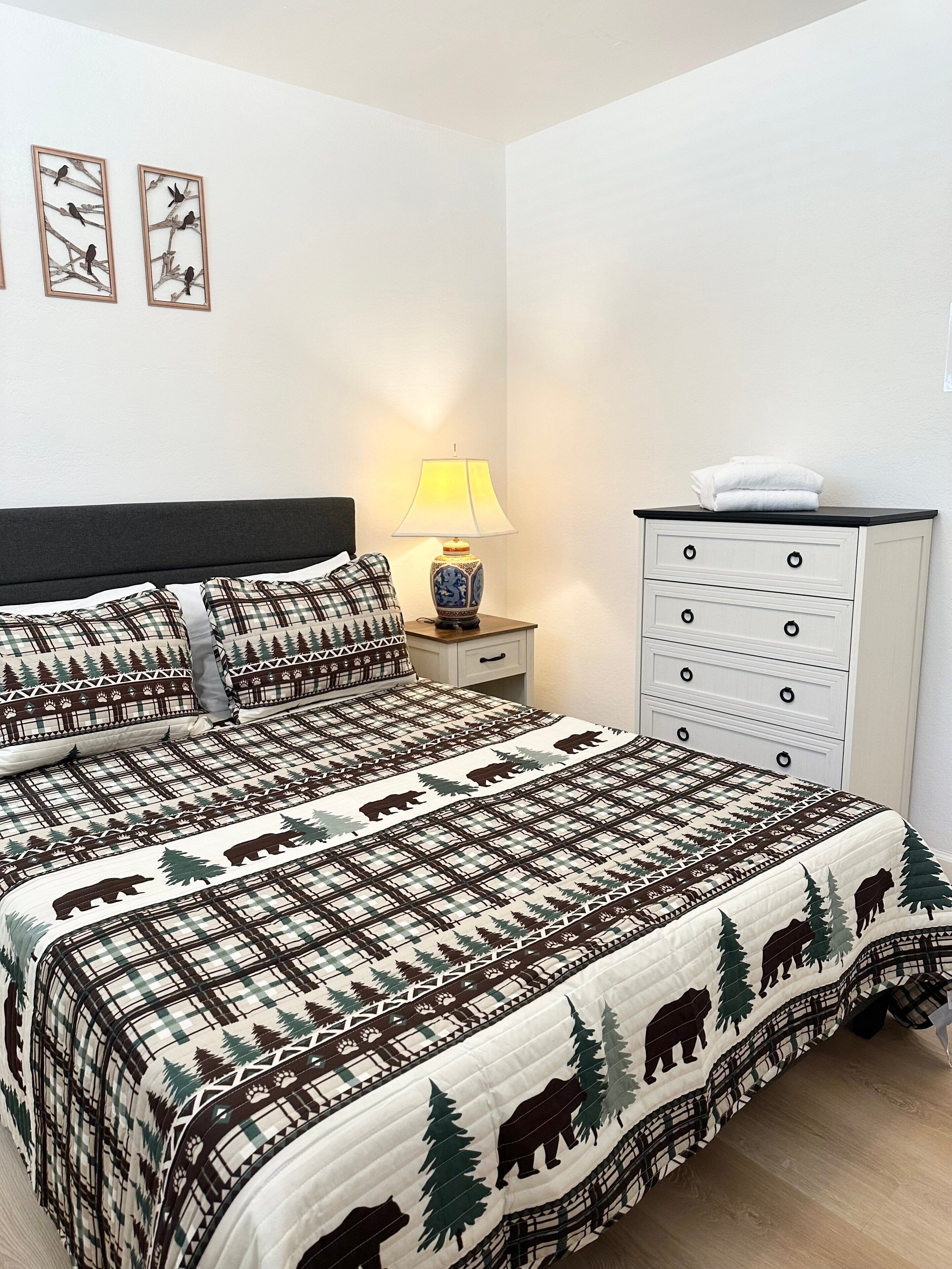 Ein Schlafzimmer mit Bett, Nachttisch mit Lampe, Kommode und Wandbildern.