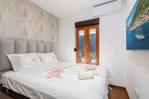 Une chambre à coucher avec un lit, une fenêtre donnant sur une ville côtière et un appareil de climatisation.
