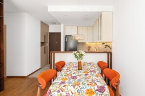 Un espace de salle à manger moderne avec une table dressée pour quatre personnes, un vase rempli de fleurs et une cuisine en arrière-plan.