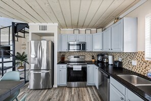 A modern kitchen with stainless steel appliances, light grey cabinets, and a checkered backsplash. - Beachfront | 3BR | Deck + Gulf Views (Galveston)