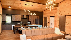 Een modern interieur met een houten plafond, een keuken met donkere kastjes, een eethoek met een lange tafel gedekt voor vier personen, en een gezellige zithoek met een bank en salontafel.