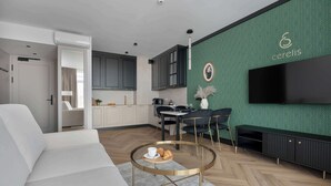 Una sala de estar moderna con un sofá, una mesa redonda de centro, un televisor montado en la pared y una cocina al fondo.