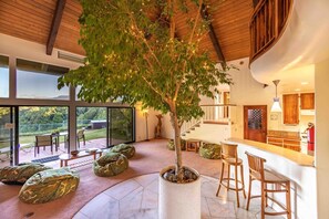 A spacious interior with a large tree, seating areas, and a kitchen. - Villa Farm Stay w/ Ocean Views on Road to Hana (Haiku)