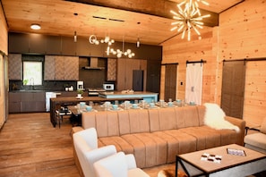 Un intérieur moderne avec un plafond en bois, une cuisine dotée de meubles sombres, un coin repas avec une longue table dressée pour quatre personnes, et un espace salon confortable avec un canapé et une table basse.