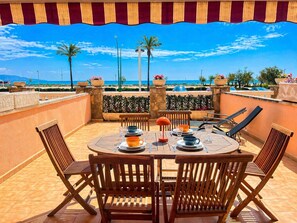 Une table ronde en bois, entourée de chaises, une lampe rouge et une vue sur la mer et les palmiers.