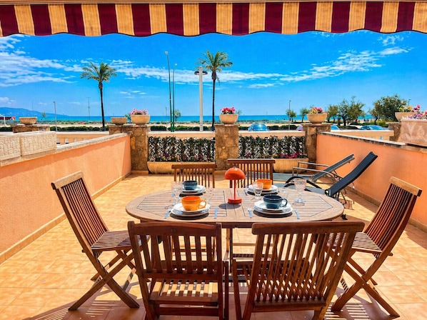 A round wooden table with chairs, a red lamp, and a view of the sea and palm trees. - 0098-MARENOSTRUM Beachfront apartment (Empuriabrava)