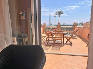 A balcony with a table and chairs, a view of the sea, and a palm tree. - 0098-MARENOSTRUM Beachfront apartment (Empuriabrava)