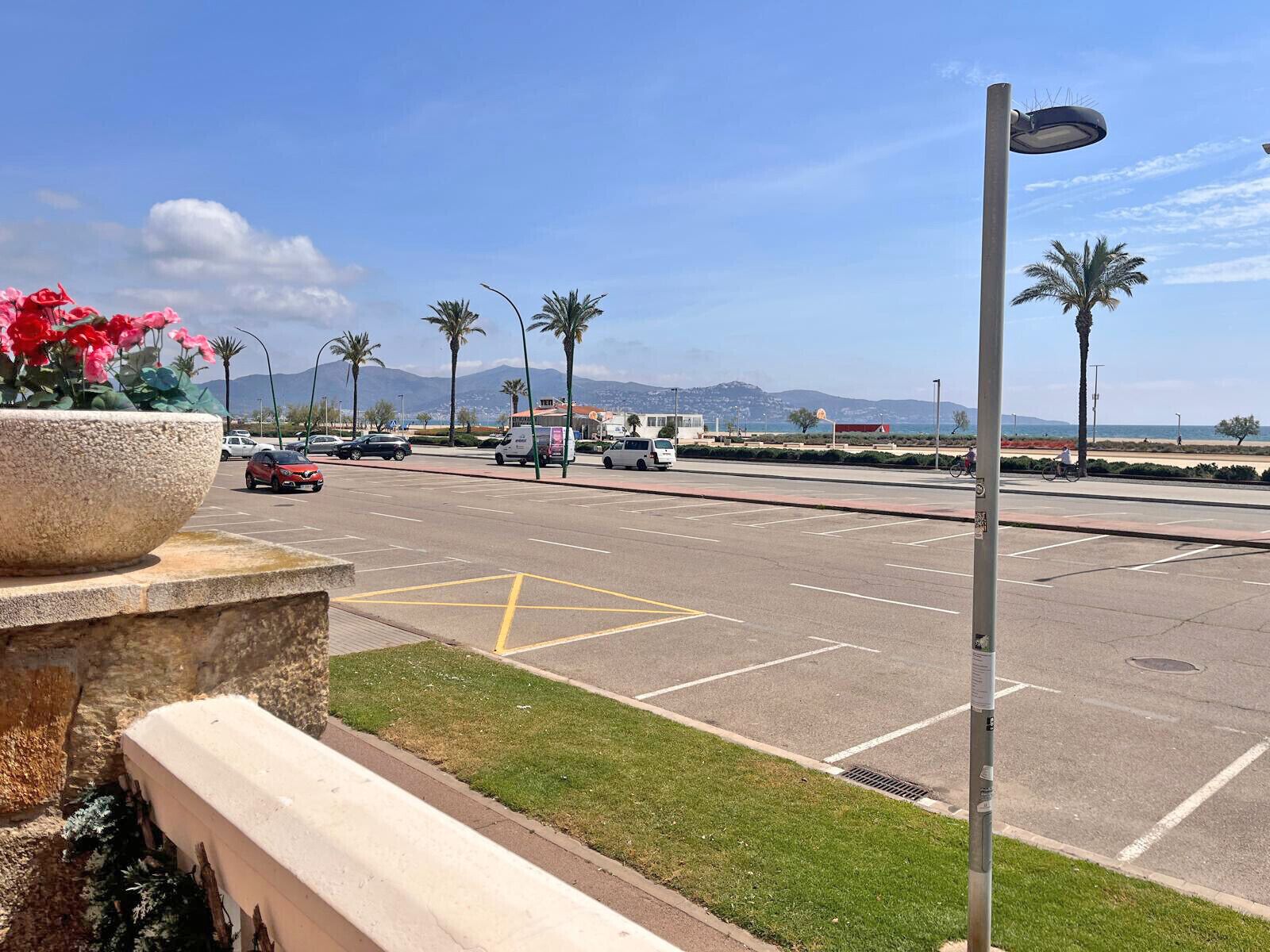 Un pàrquing amb places delimitades, un carrer amb vehicles i un cel serè.