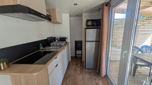 Een compacte keuken met een zwart aanrechtblad, roestvrijstalen apparatuur en een schuifpui naar een buitenruimte.
