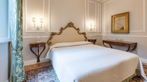 Een slaapkamer met een groot bed, een versierd hoofdeinde, wandlampen, een spiegel en een kroonluchter.
