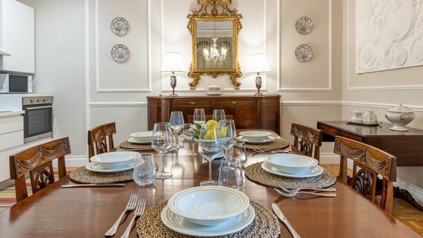 Een eetkamer met een houten tafel voor zes personen, een kroonluchter en een decoratieve spiegel boven de tafel.