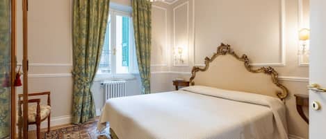 A bedroom with a large bed, a chandelier, a window with curtains, and a radiator.