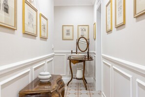 Un couloir orné de tableaux encadrés, un meuble en bois, un miroir et un lavabo avec un support décoratif.