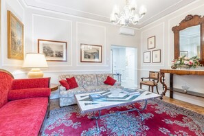 Ein Wohnzimmer mit einem roten Sofa, einem gemusterten Sofa, einem Couchtisch, einer Lampe und gerahmten Bildern an den Wänden.