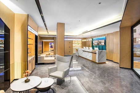 A modern hotel lobby with a reception desk, seating area, and a view of the street.