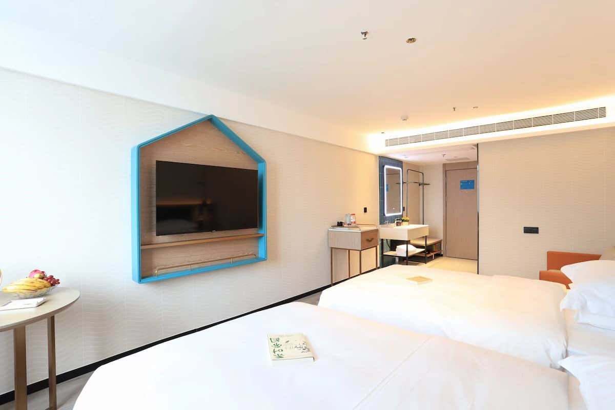 Habitación de hotel con dos camas, una mesita con fruta, un espejo y un escritorio con lámpara.