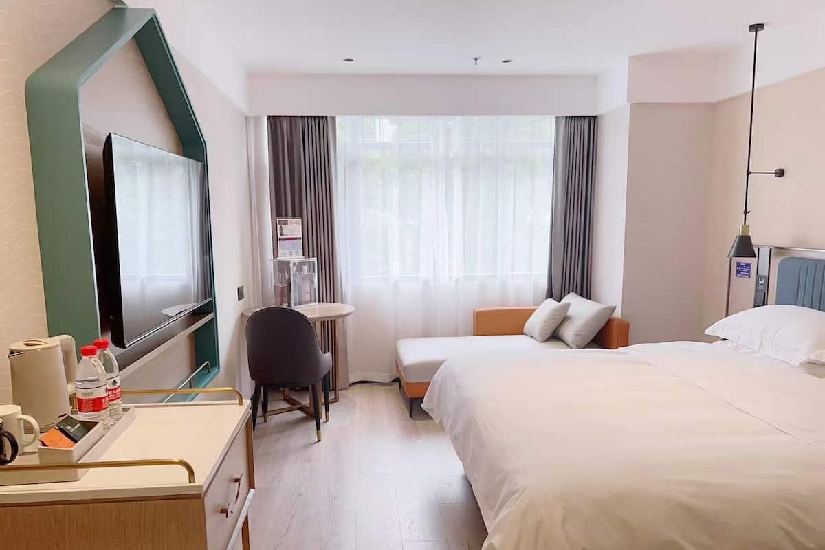 Habitación de hotel con cama, mesita de noche, silla, escritorio, televisor y cortinas.