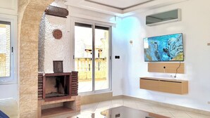A living room with a fireplace, a TV mounted on the wall, and a glass coffee table. - Spacious 6-bedroom villa in gorgeous Tangier with pool (Tangier)