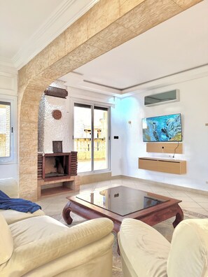 A living room with a fireplace, a TV mounted on the wall, and a glass coffee table. - Spacious 6-bedroom villa in gorgeous Tangier with pool (Tangier)
