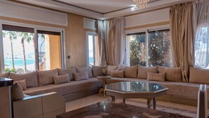 A modern living room with a sectional sofa, a glass coffee table, and large windows with curtains. - Spacious 6-bedroom villa in gorgeous Tangier with pool (Tangier)