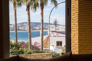 A coastal view with palm trees, a beach, and a cityscape.