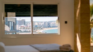 A room with a bed, a window with blinds, and a view of a beach and cityscape. - Spacious 6-bedroom villa in gorgeous Tangier with pool (Tangier)
