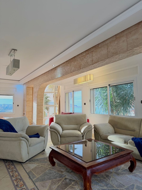 A spacious living room with a high ceiling, large windows, and a view of the outdoors.