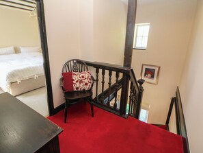 A bedroom with a bed, a chair with a patterned cushion, a red carpeted staircase, and a framed picture on the wall. - Pine Cottage (Hope Valley)