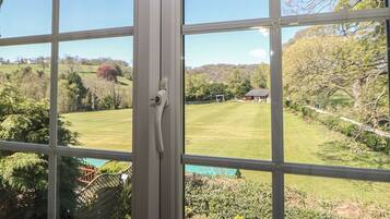 A view through a window with a white frame, a door handle, and a clear view of a green lawn, trees, and a distant building.