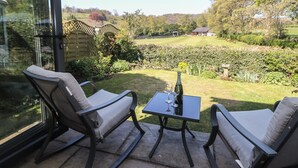 A patio with two rocking chairs and a table, overlooking a garden with a vineyard. - Pine Cottage (Hope Valley)