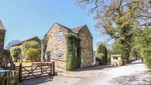 A stone building with a gated entrance, a paved driveway, and surrounding greenery. - Pine Cottage (Hope Valley)
