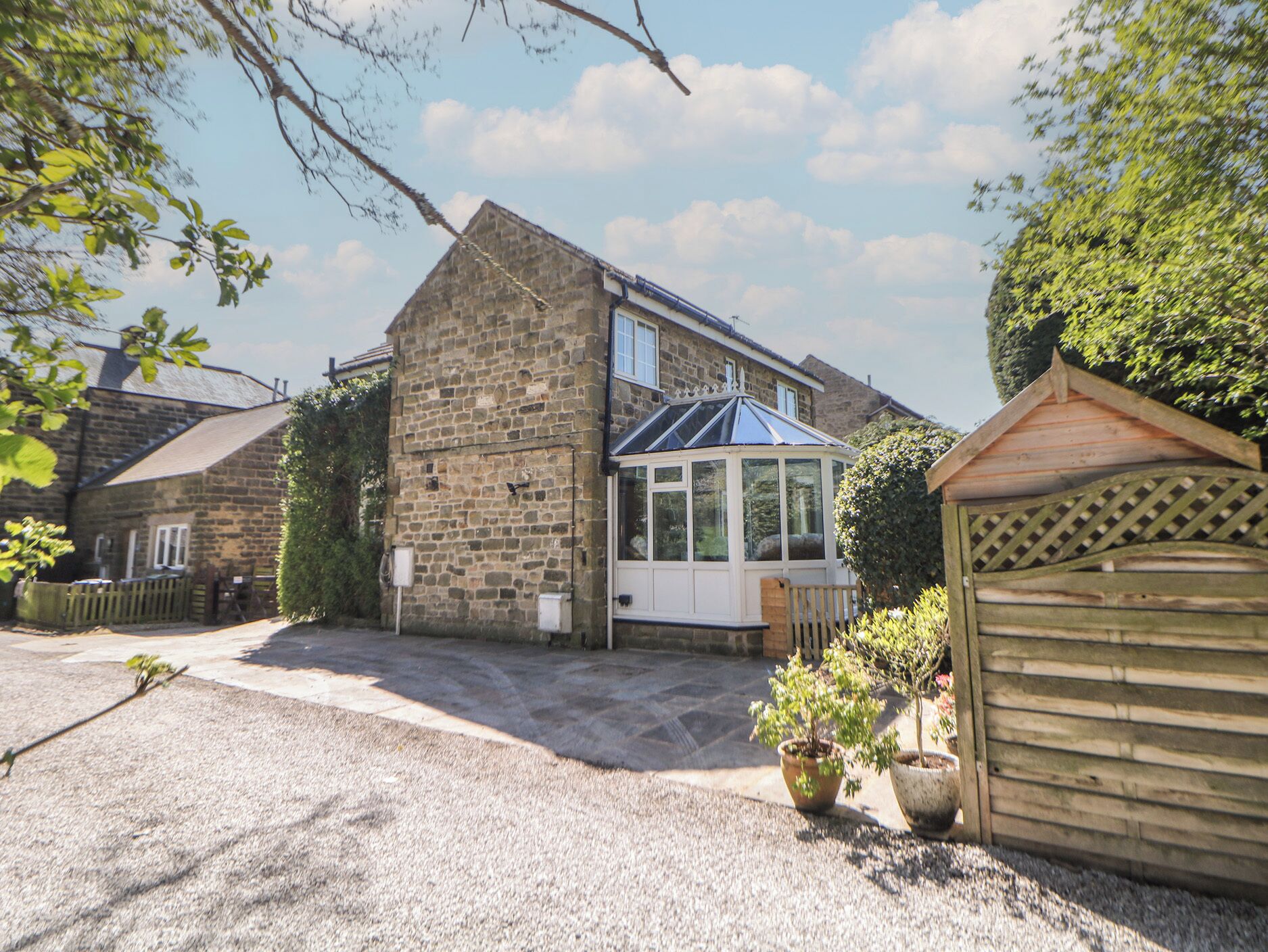 A stone house with a conservatory, gravel driveway, and a wooden gate.
