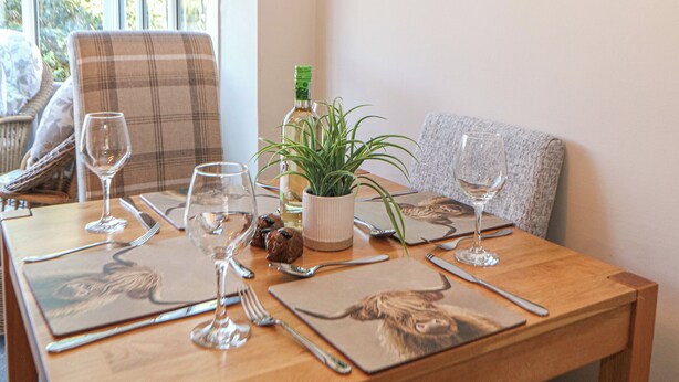 A dining table set with wine glasses, cutlery, and a bottle of wine, with a plant and a decorative plate in the center. - Pine Cottage (Hope Valley)