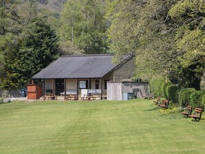 A small building with a sloped roof, a porch with benches, and a sign indicating a cricket club. - Pine Cottage (Hope Valley)