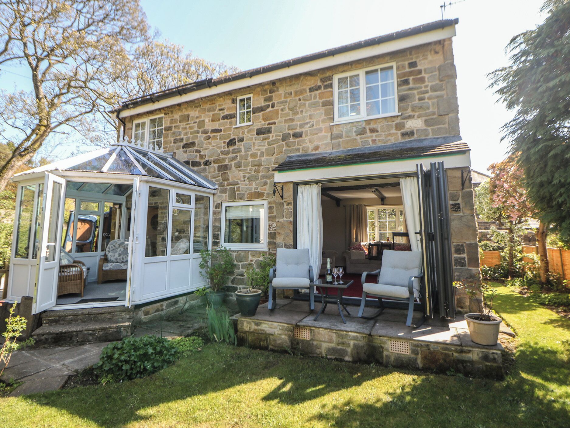 A stone house with a conservatory, a patio with outdoor seating, and a garden.