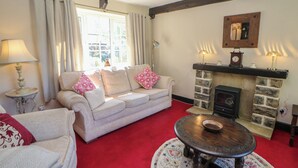A cozy living room with a sofa, a round wooden table, a fireplace, and a window with curtains. - Pine Cottage (Hope Valley)