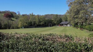 A grassy field with a building, trees, and a hill in the background. - Pine Cottage (Hope Valley)