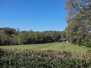 Ein grünes Feld mit einem Gebäude, Bäumen und einer Hügelkette im Hintergrund.