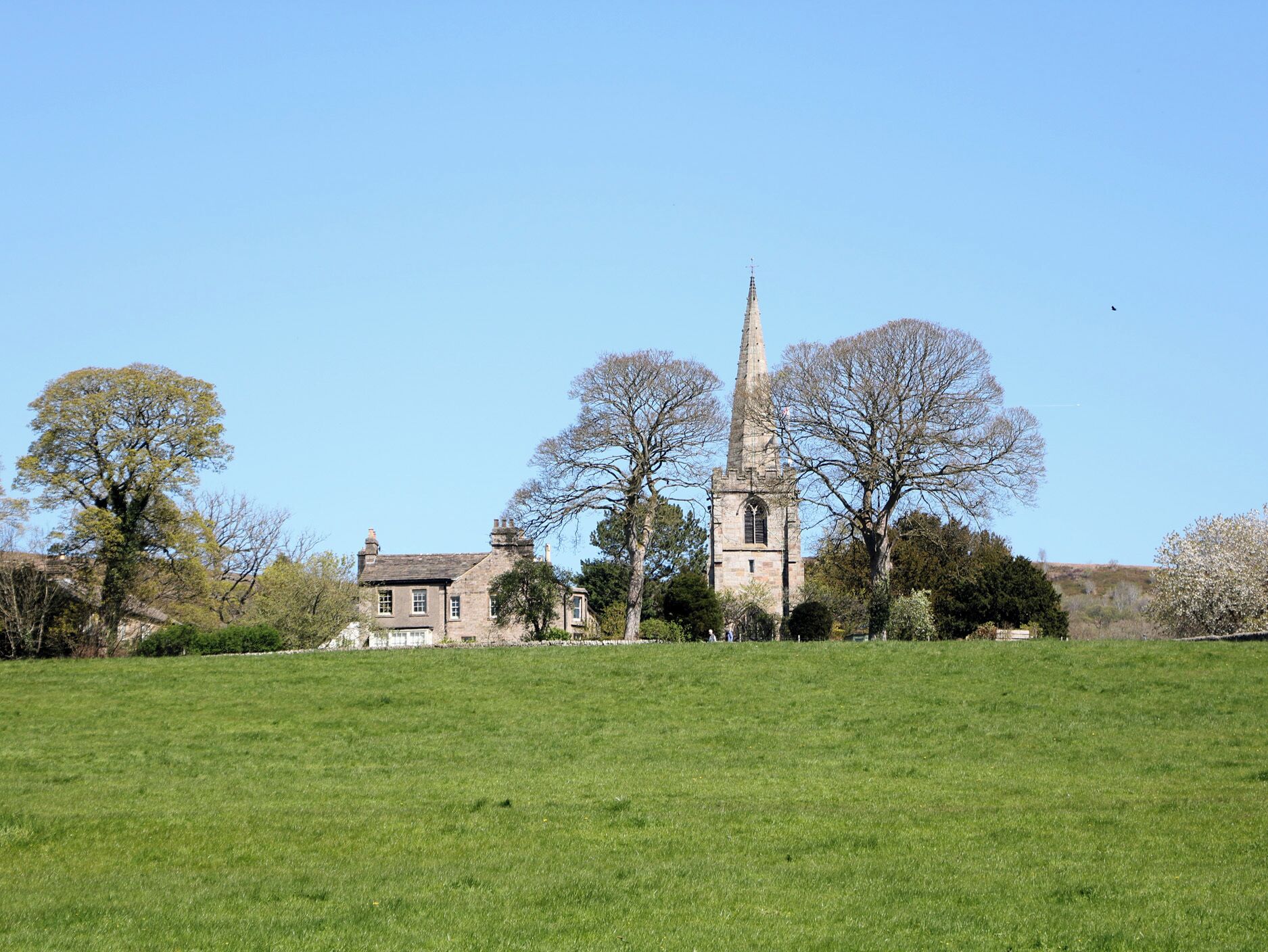 A church with a tall spire, surrounded by a grassy field and trees.