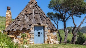 A stone cottage with a thatched roof, a blue door, and a stone chimney. - BeLocations - Villa VERDALMA (Sardegna)