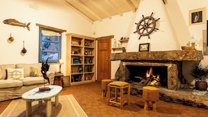 A cozy living room with a fireplace, wooden shelves, and a sofa. - BeLocations - Villa VERDALMA (Sardegna)