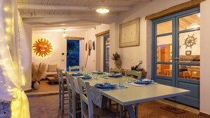 A dining area with a long table, chairs, and a view through a window. - BeLocations - Villa VERDALMA (Sardegna)