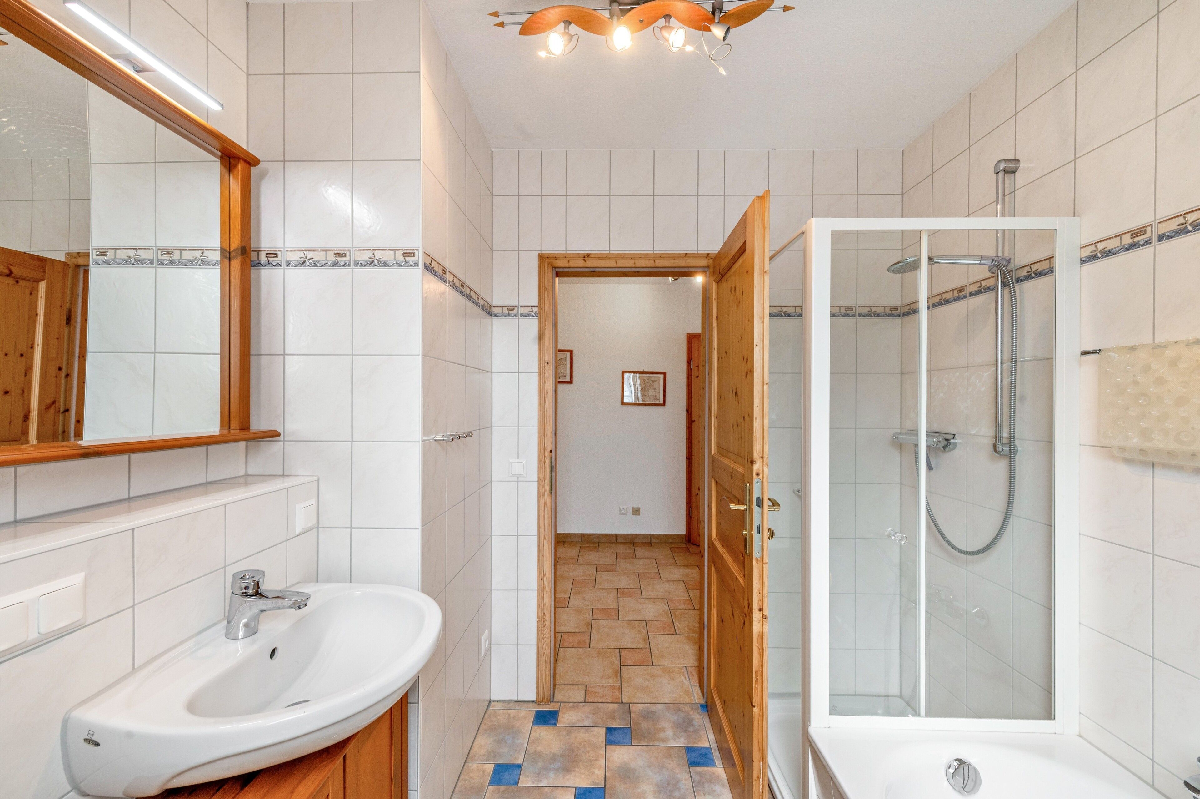 Een badkamer met een wastafel, spiegel, douche en betegelde vloer.