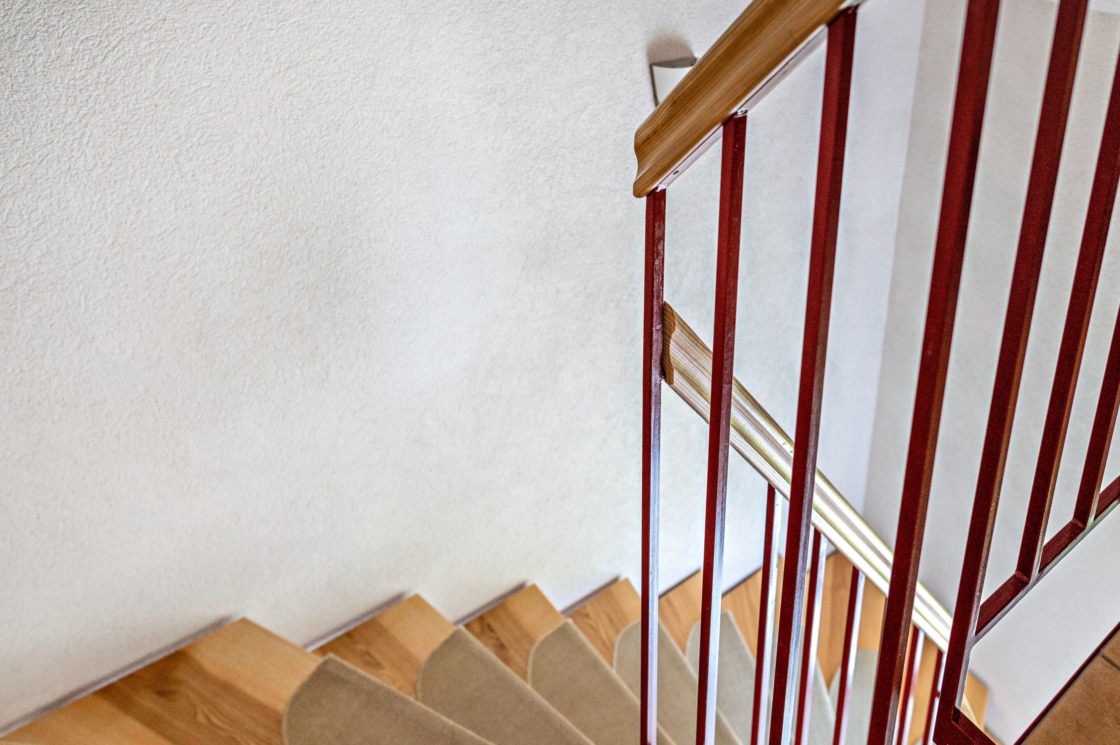Eine Holztreppe mit roter Handlaufstange und beigefarbenen Teppichstufen.